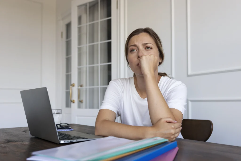 Jeune femme préoccupée devant un ordinateur portable, illustrant l’incertitude professionnelle liée à la perte d’emploi à l’étranger.
