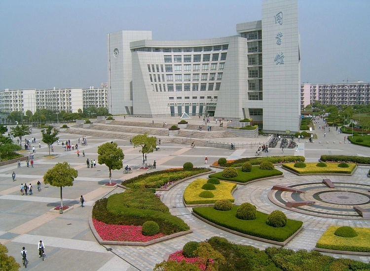 Vue extérieure d’un bâtiment universitaire moderne avec une grande esplanade et des jardins aménagés, étudiants marchant et circulant à vélo sur le campus.