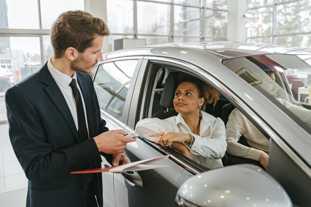 Une femme assise dans une voiture discutant des détails avec un vendeur de voitures en costume, illustrant le processus d'achat d'une voiture en Thaïlande.