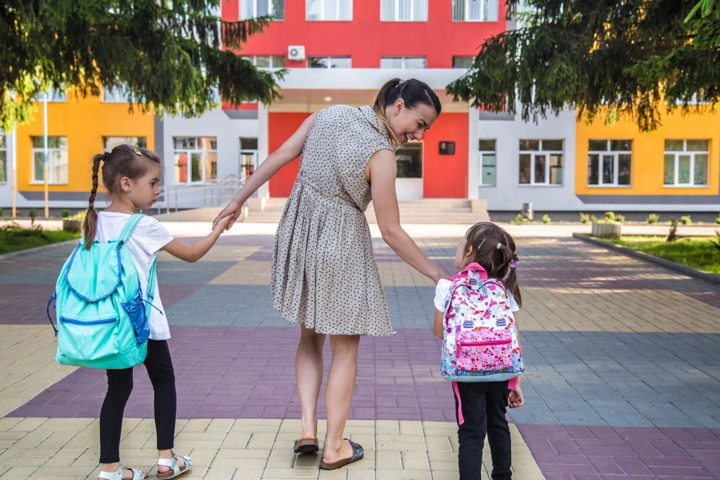 Deux jeunes élèves entrant dans une école primaire colorée avec leur mère, une scène quotidienne dans le système scolaire en Espagne.
