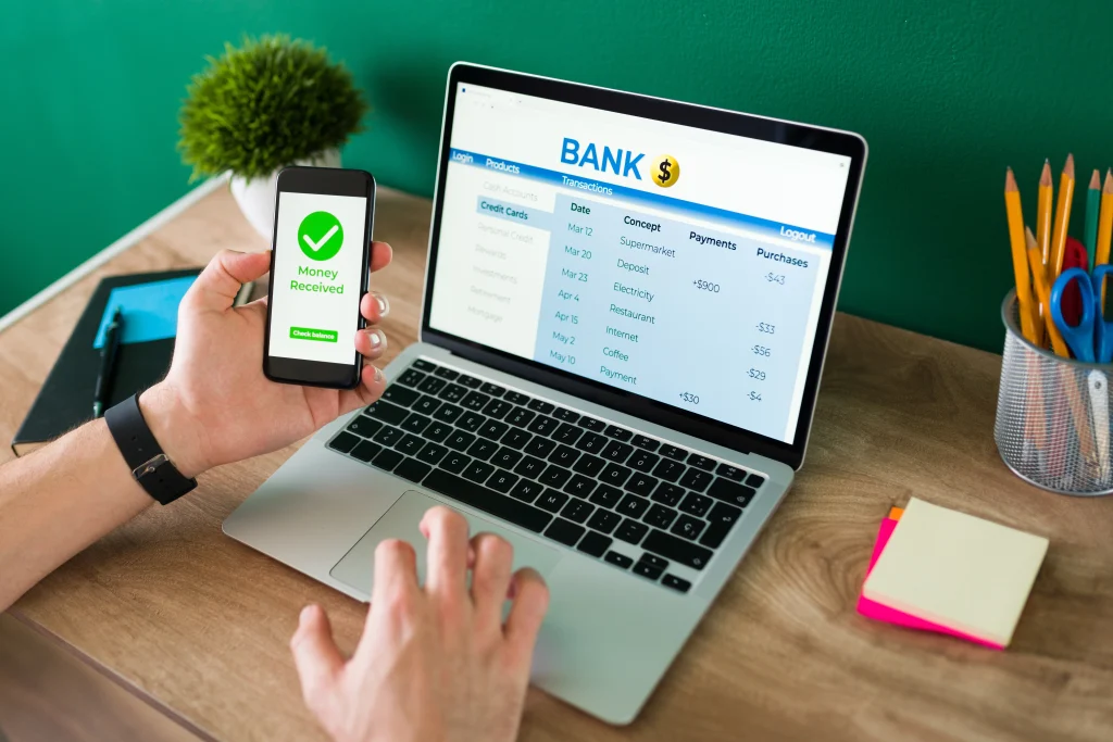 Man using smartphone and laptop for online banking and receiving an international money transfer.
