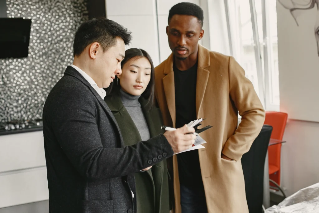 Jeune couple multiculturel signant un contrat immobilier avec un agent, représentant les étapes clés pour acheter une maison au Japon.