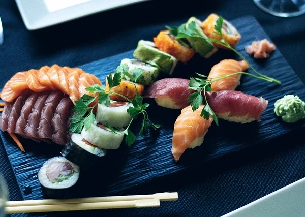 Plateau de sushis avec sashimi, nigiri et makis, joliment présenté avec persil et wasabi sur une assiette ardoise.