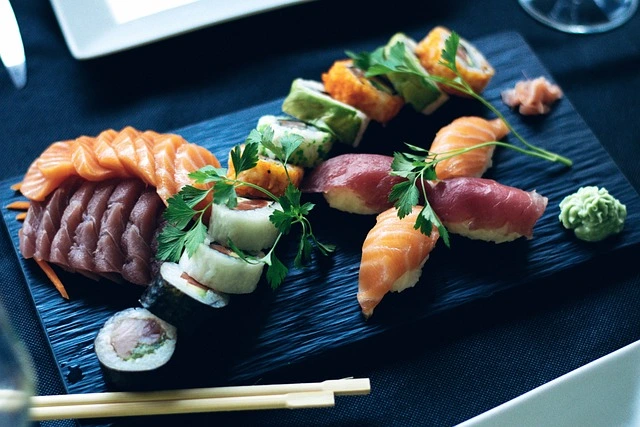 Plateau de sushis avec sashimi, nigiri et makis, joliment présenté avec persil et wasabi sur une assiette ardoise.