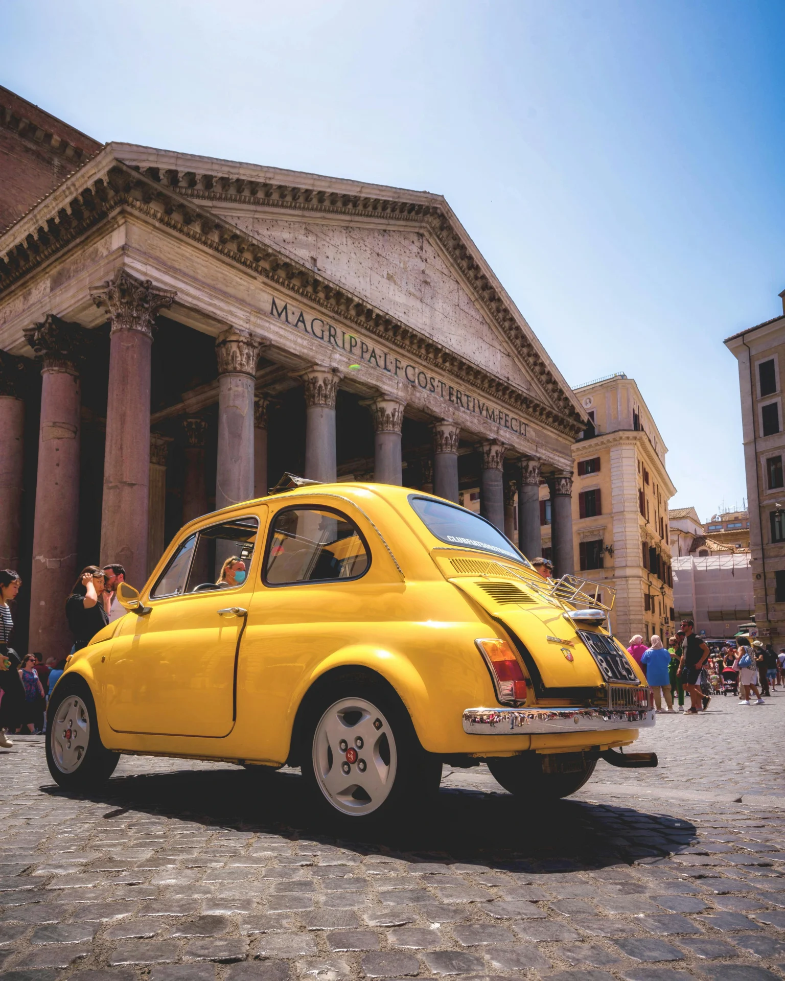 Renting a car in Italy lets you explore historic sites like the Pantheon in Rome, seen here with a classic yellow Fiat 500 parked on cobblestone streets.