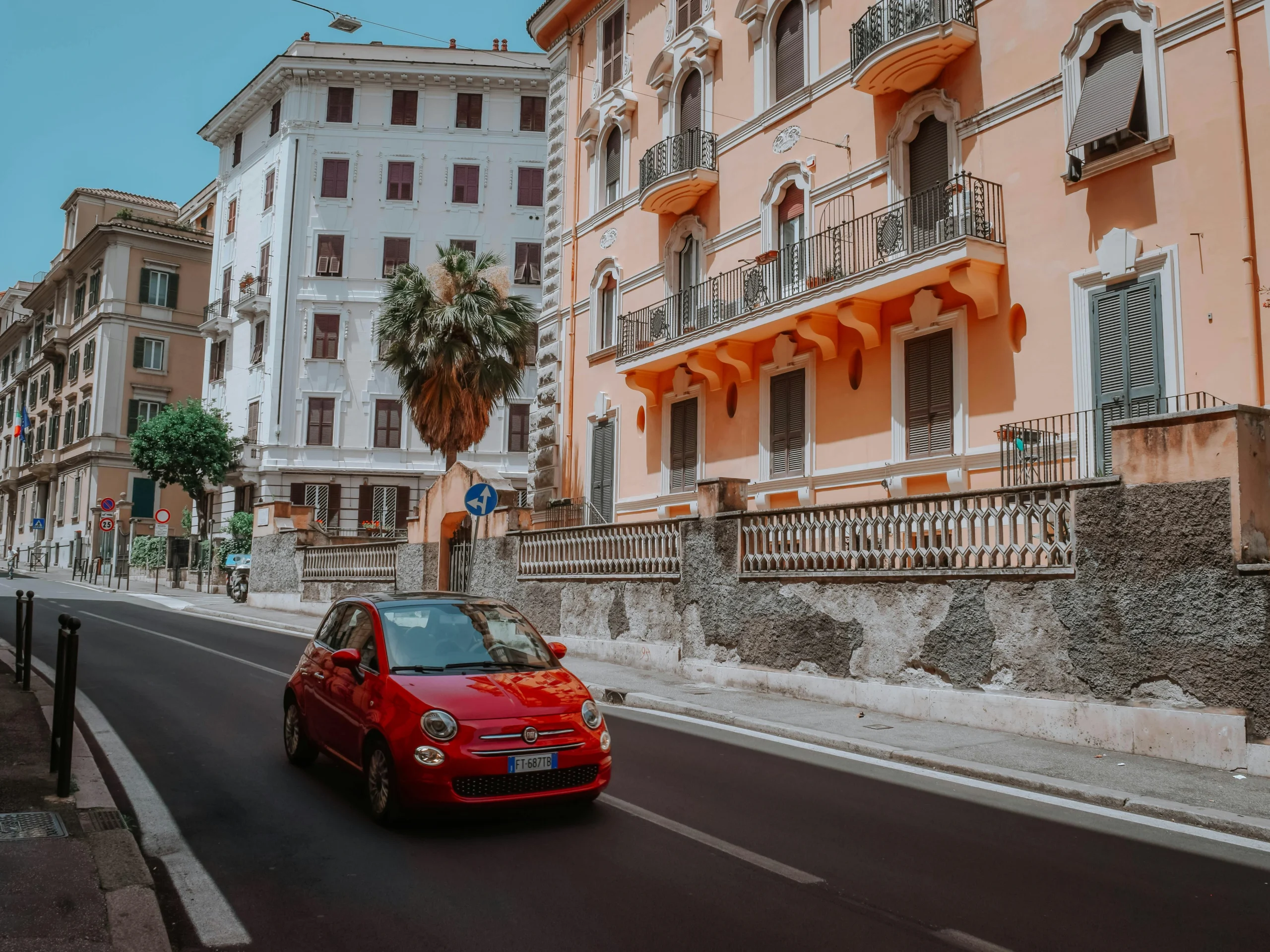Renting a car in Italy allows you to drive through charming streets, as seen with this red Fiat 500 navigating past pastel-coloured buildings in Rome.