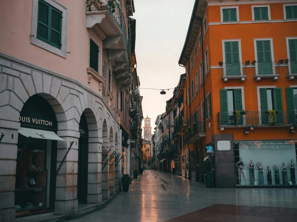 A picturesque Italian street with traditional architecture and boutique shops, representing the vibrant lifestyle in Italy’s residential areas. Exploring different neighbourhoods is essential when Renting in Italy to find the perfect accommodation.