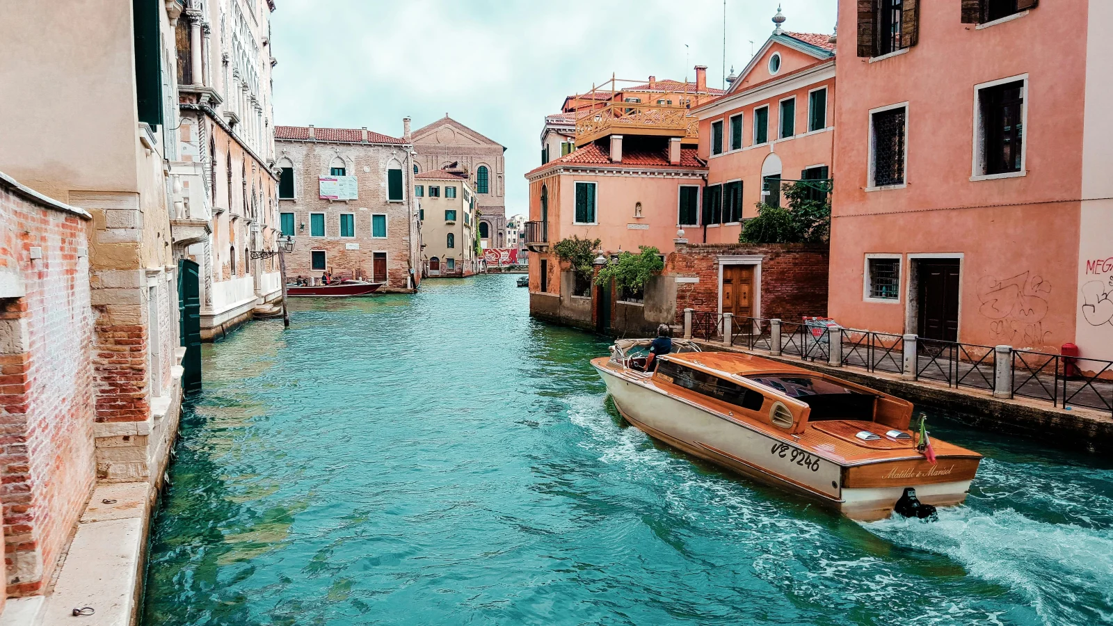 A stunning canal view in Venice with a wooden boat passing through historic buildings, showcasing the charm of Italian accommodation. Discover how Renting in Italy offers unique housing experiences, from Venetian apartments to countryside villas.