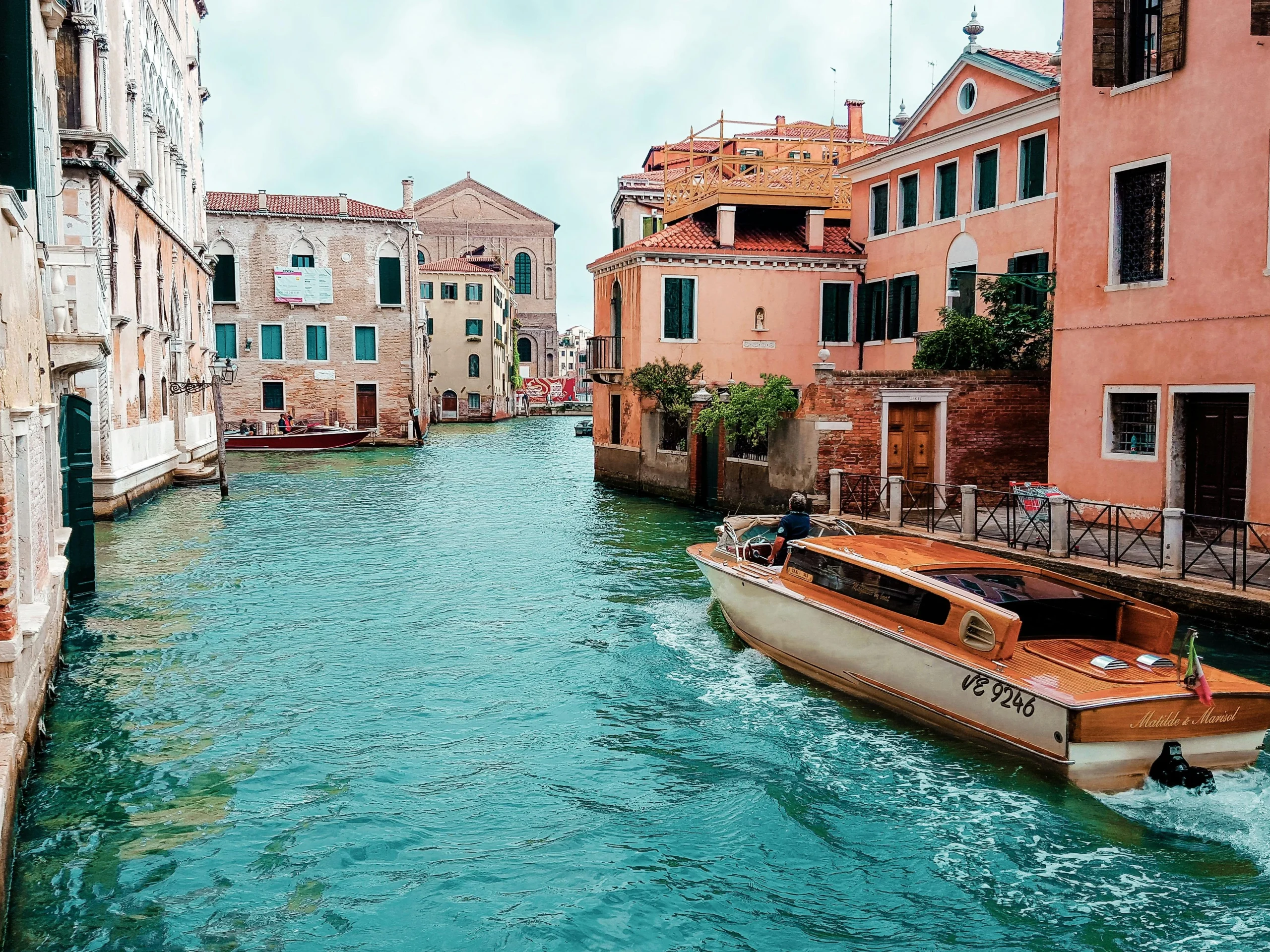 A stunning canal view in Venice with a wooden boat passing through historic buildings, showcasing the charm of Italian accommodation. Discover how Renting in Italy offers unique housing experiences, from Venetian apartments to countryside villas.