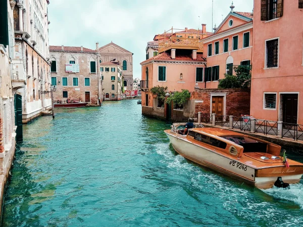 A stunning canal view in Venice with a wooden boat passing through historic buildings, showcasing the charm of Italian accommodation. Discover how Renting in Italy offers unique housing experiences, from Venetian apartments to countryside villas.