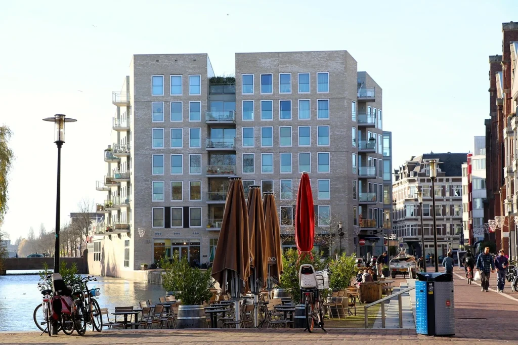 Modern apartments and outdoor café by a canal in Amsterdam's Oud-West, showcasing the area's relaxed and stylish atmosphere to stay in Amsterdam