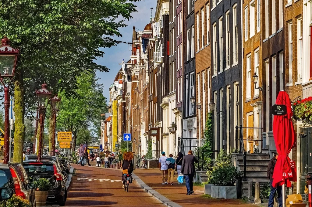 Charming street in Amsterdam with traditional townhouses, trees, and cyclists – showcasing the beauty of the best neighborhoods to stay in the city.