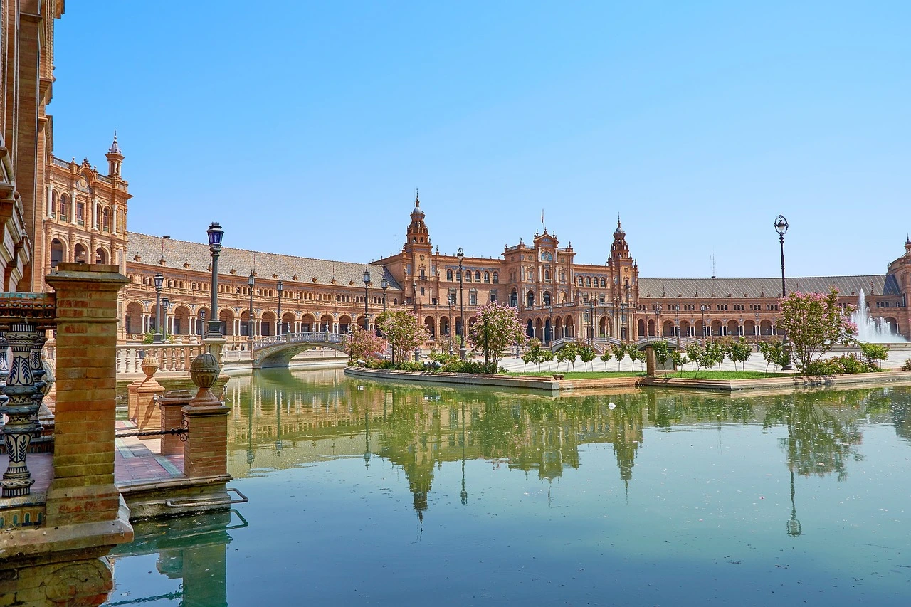 The majestic Plaza de España in Seville, featuring a grand semi-circular building, bridges over the canal, and detailed tilework reflecting Andalusian charm.