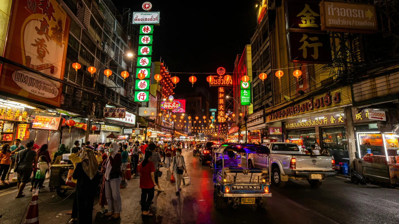 A vibrant night market in Thailand filled with street food stalls, neon signs, and tuk-tuks. A must-visit spot to experience the best foods in Thailand.