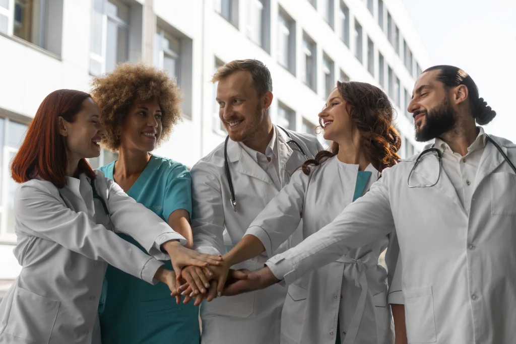 Smiling doctors and nurses joining hands in teamwork outside a modern hospital, symbolizing collaboration, diversity, and dedication in the medical field.
