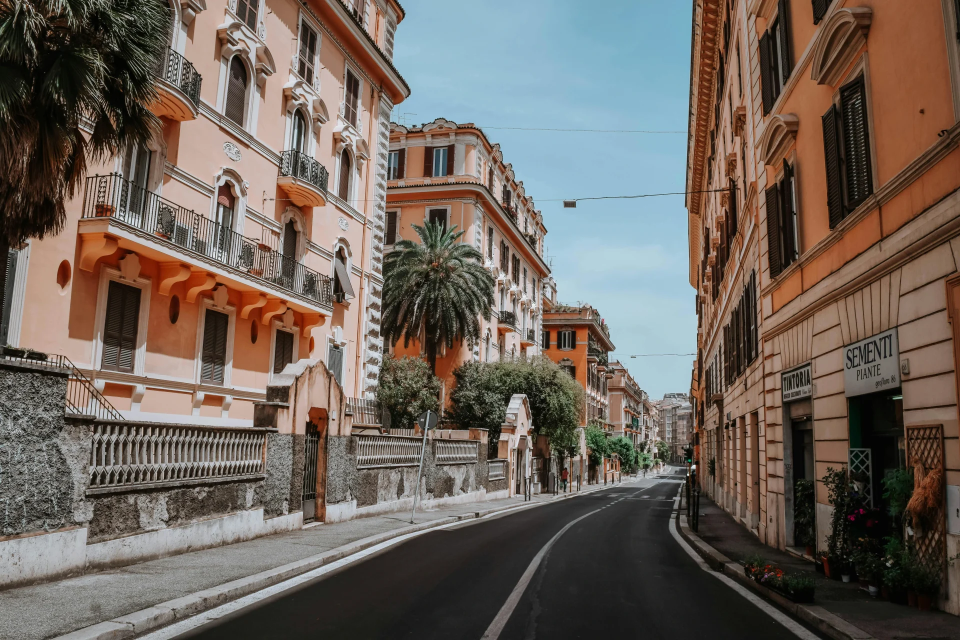A quiet, picturesque street in Rome lined with historic buildings, palm trees, and charming balconies, capturing the city's timeless architectural beauty.