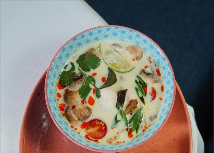 A bowl of Tom Kha Gai, a creamy coconut soup with chicken, lime, mushrooms, and herbs, served with jasmine rice. One of the best foods in Thailand.