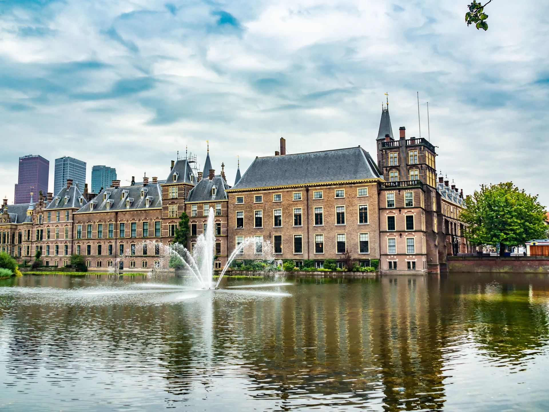 A grand historic building with a fountain in front, showcasing classic European architecture with a mix of modern cityscape in the background.