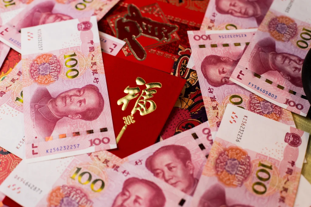 Billets de 100 yuans chinois entourant une enveloppe rouge traditionnelle avec des caractères dorés, symbolisant la prospérité et la chance durant le Nouvel An lunaire.