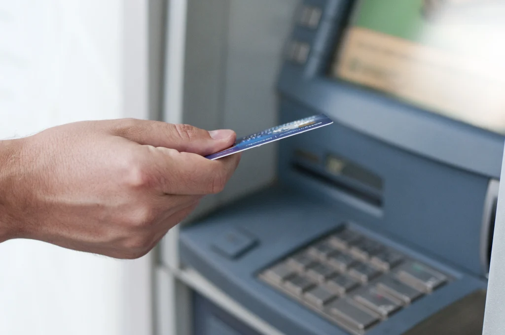 Une personne insère une carte bancaire dans un distributeur, illustrant l’accès facile à l’argent liquide via un compte bancaire en Indonésie.