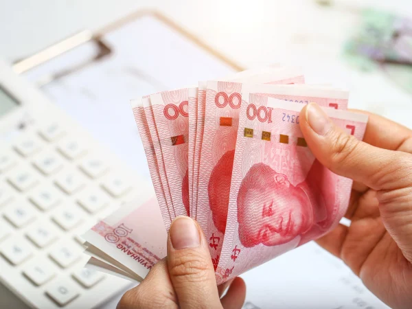 Personne comptant des billets de yuan chinois avec une calculatrice en arrière-plan, symbolisant le calcul des salaires et les impôts en Chine pour les expatriés.