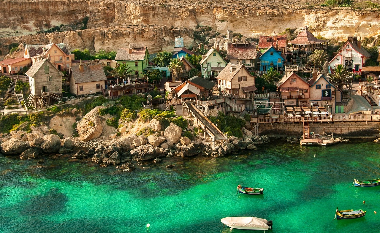 Village côtier coloré à Malte avec de l'eau turquoise, mettant en valeur des vues pittoresques et montrant comment le coût de la vie à Malte inclut l'accès à des lieux uniques comme celui-ci.