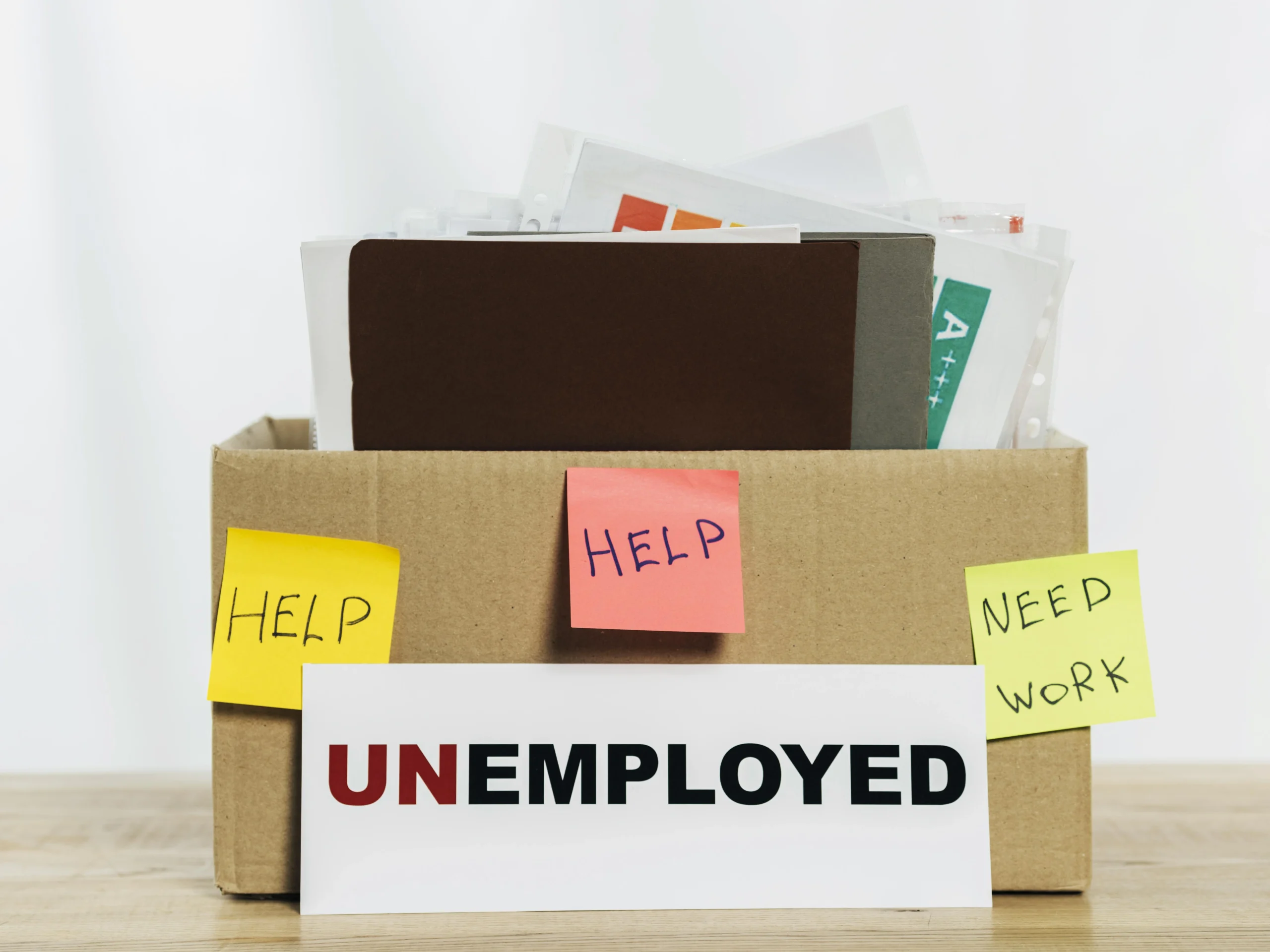Unemployment in Italy visualized by a cardboard box labelled UNEMPLOYED with documents and help notes after job loss.
