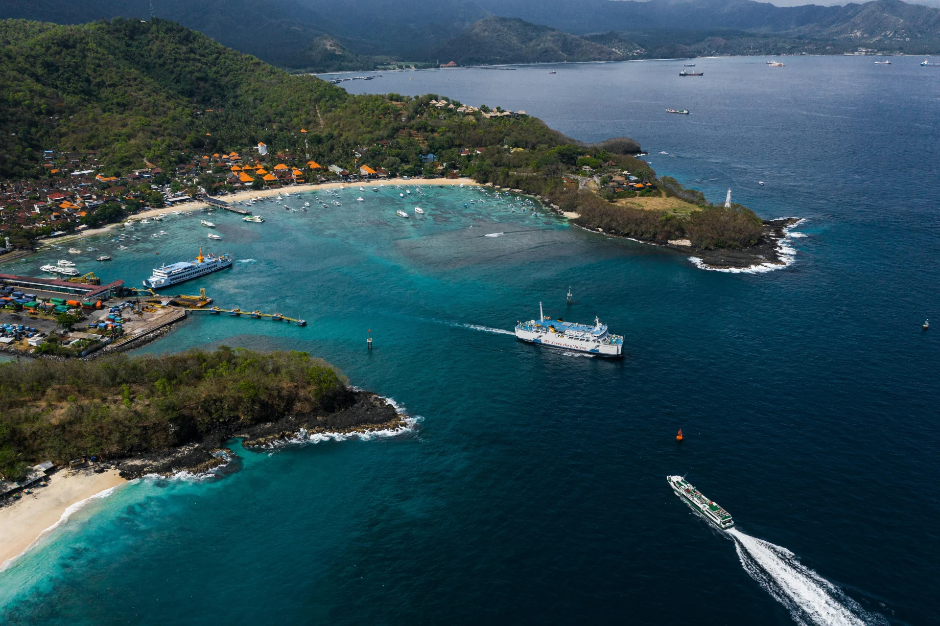 Vue aérienne du port de Padangbai à Bali avec ses ferries, bateaux et eaux turquoise, mettant en avant le transport côtier et les paysages maritimes de l’île.