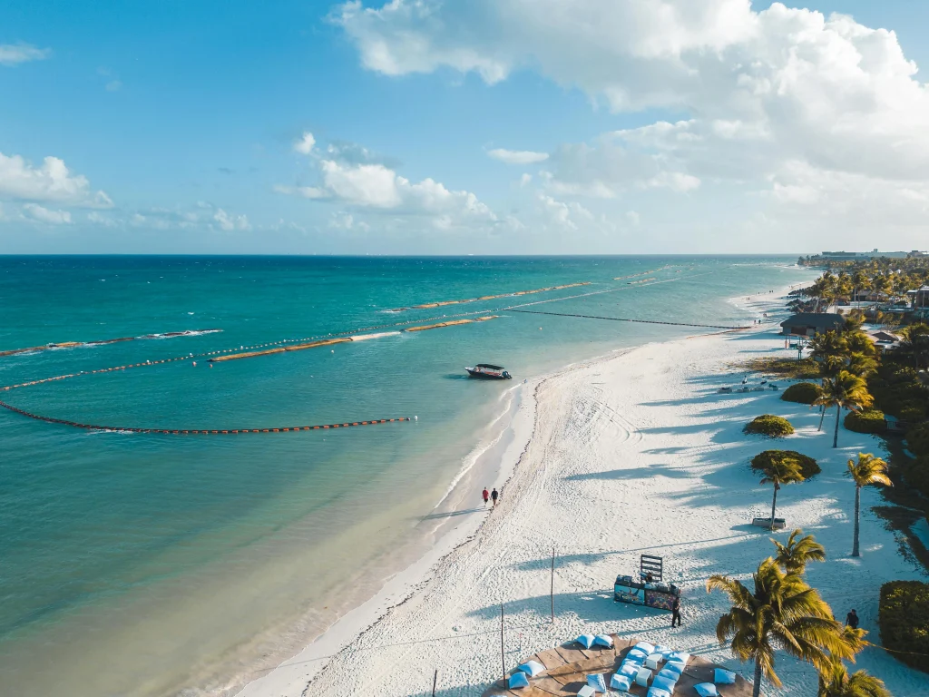 Plages de sable blanc et eaux turquoise de Playa del Carmen, bordées de complexes hôteliers et de palmiers.