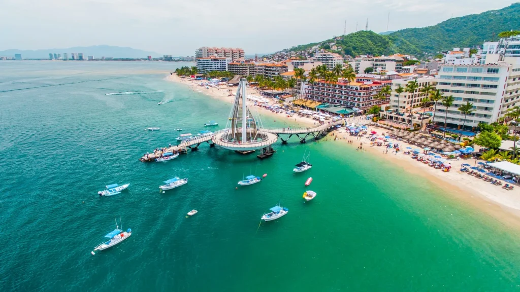 Bateaux flottant près de la jetée de Los Muertos à Puerto Vallarta, avec des plages animées et des hôtels en arrière-plan.