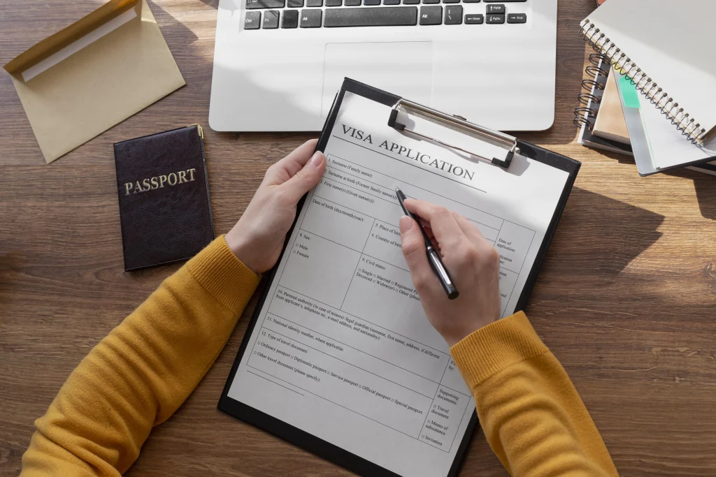 Person completing a Visa in Colombia application form on a clipboard with a passport and laptop on a desk.