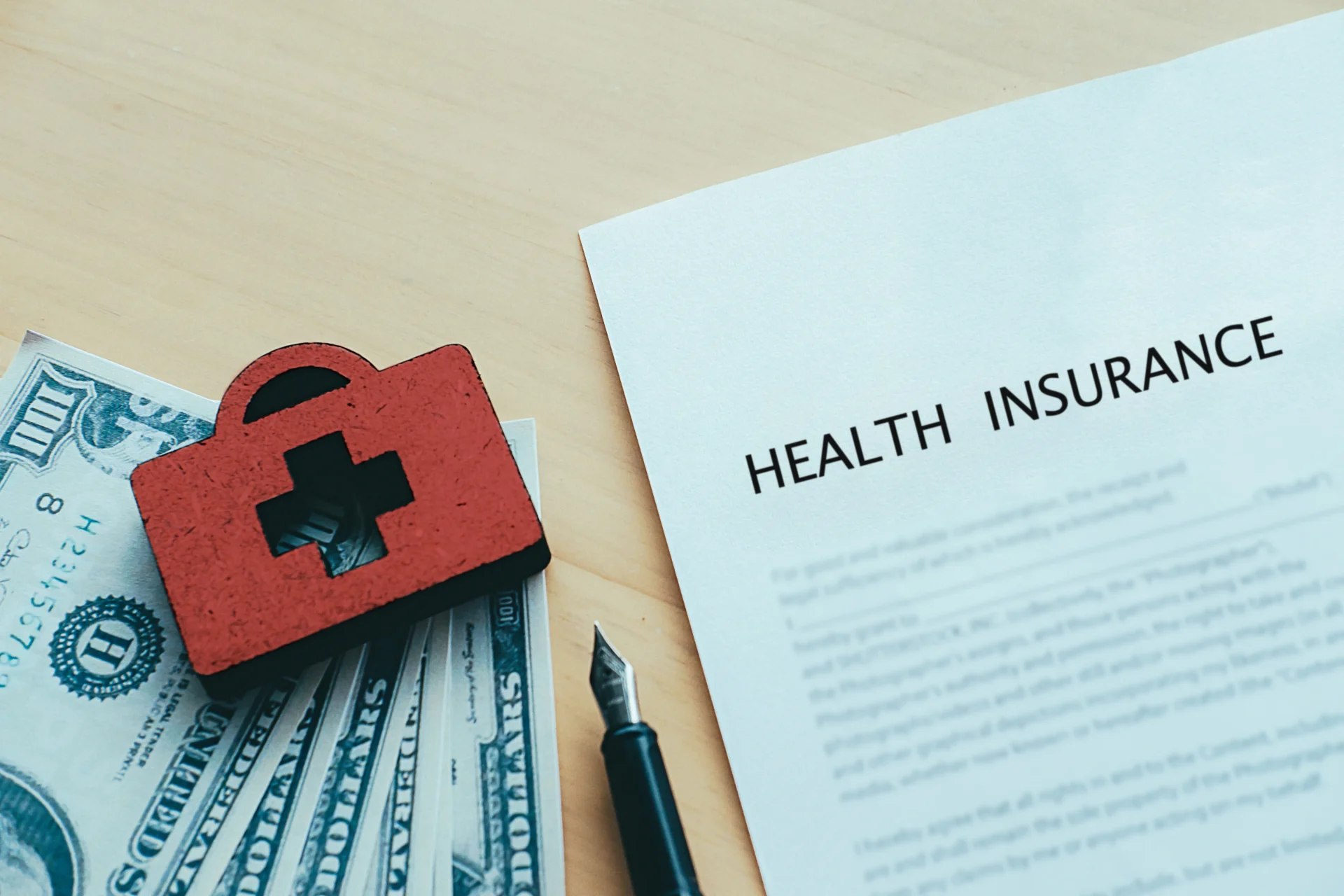 Le système de santé en Suisse illustré par un document d’assurance santé, des billets en dollars et un symbole médical rouge suisse sur un bureau.