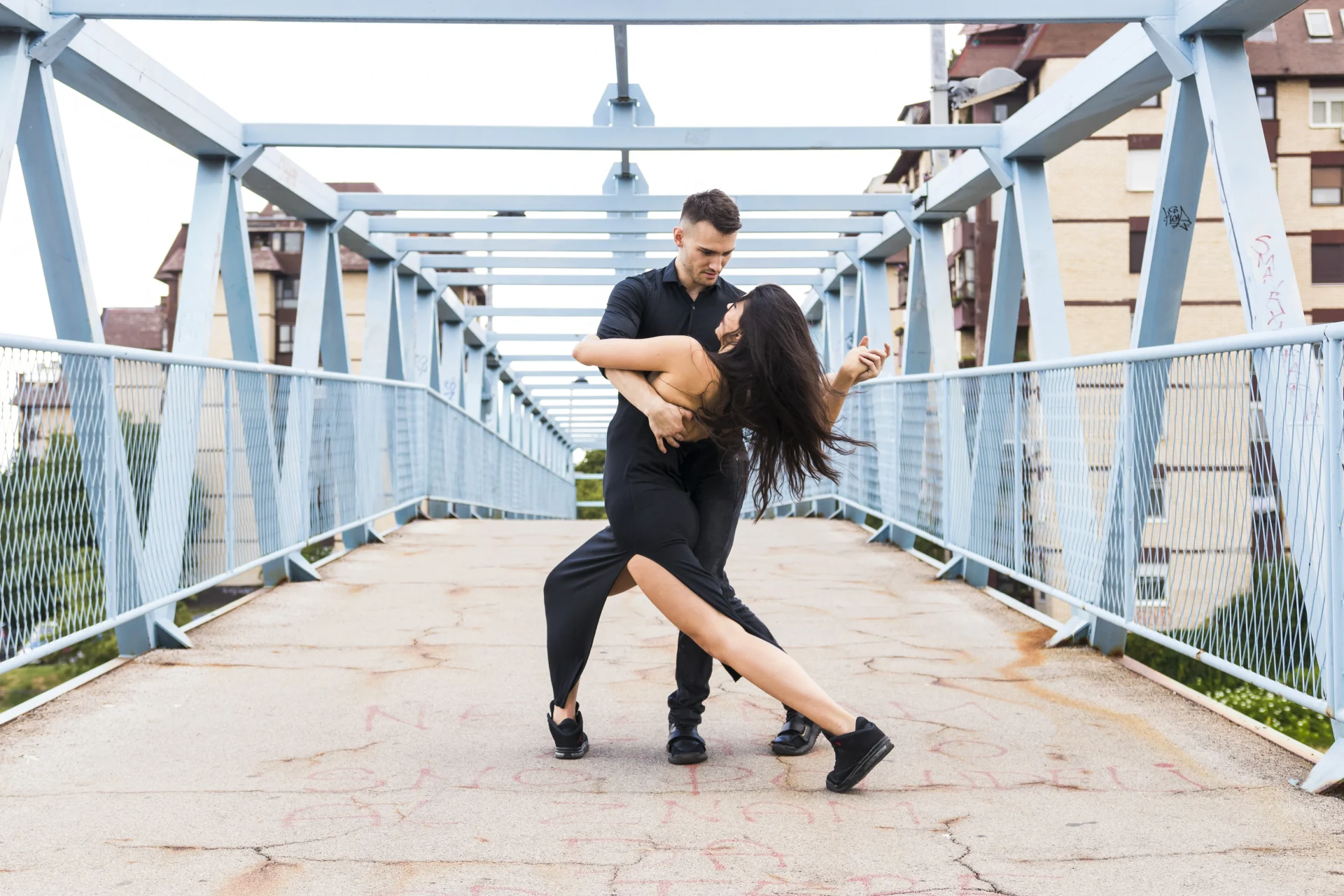 Un couple danse passionnément sur une passerelle moderne, mêlant paysage urbain et mouvement expressif en parfaite harmonie.