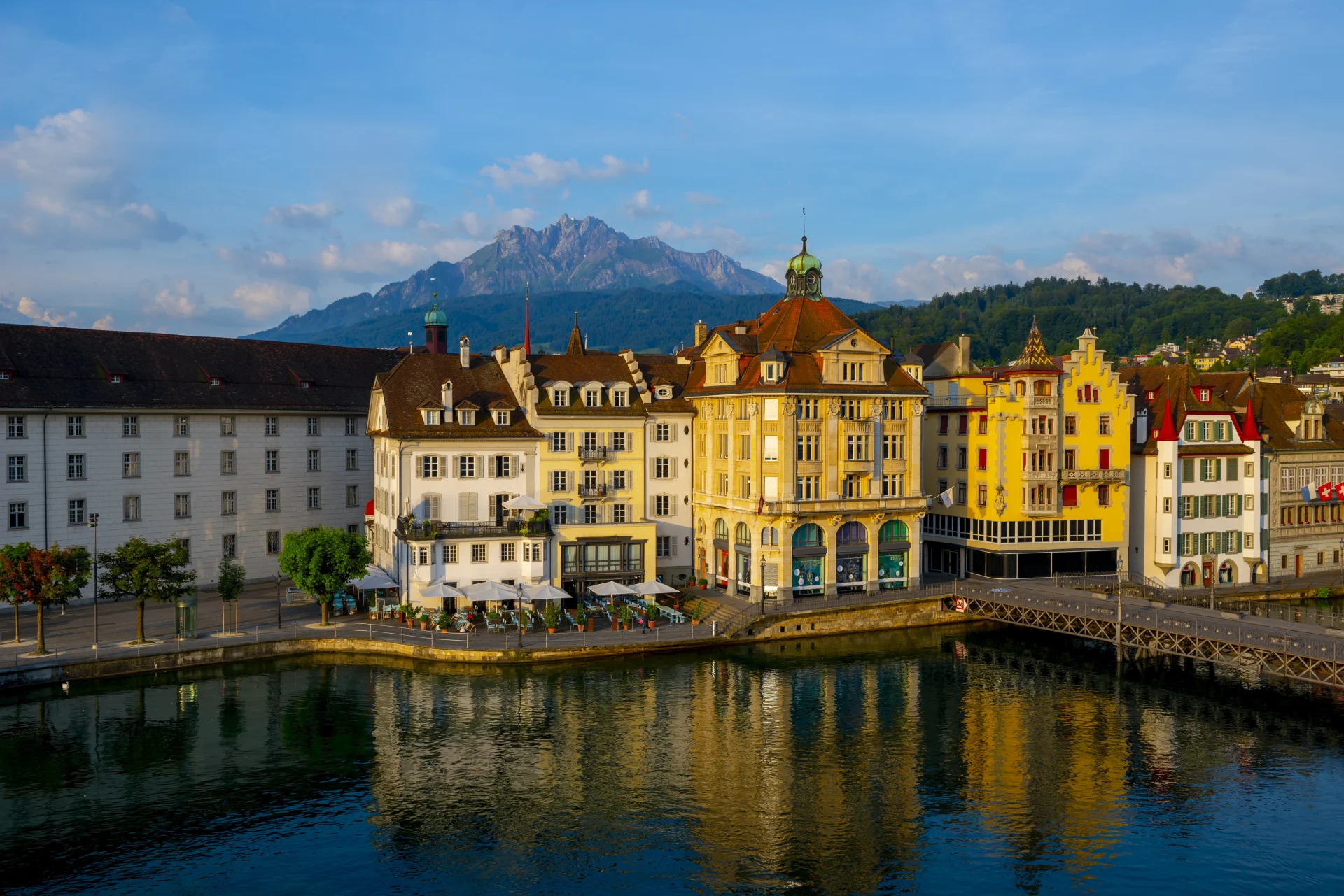 Colorful historic buildings along the waterfront in Lucerne, Switzerland, with Mount Pilatus in the background on a sunny day.