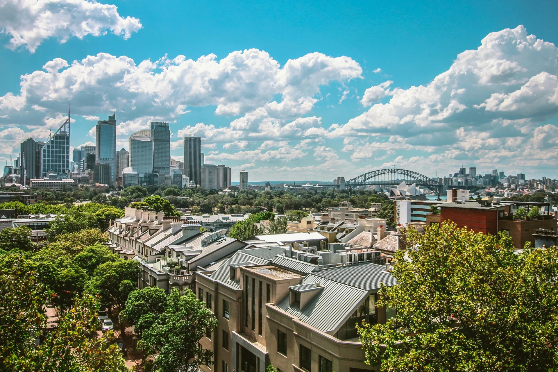 Vue sur la skyline de Sydney avec le Harbour Bridge et l’Opéra en arrière-plan, depuis un quartier résidentiel verdoyant.