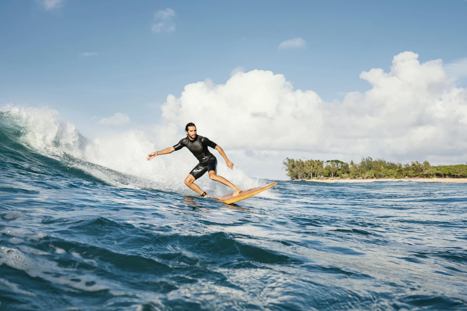 Homme surfant une vague près des côtes australiennes par une journée ensoleillée, avec ciel bleu et arbres tropicaux en arrière-plan.