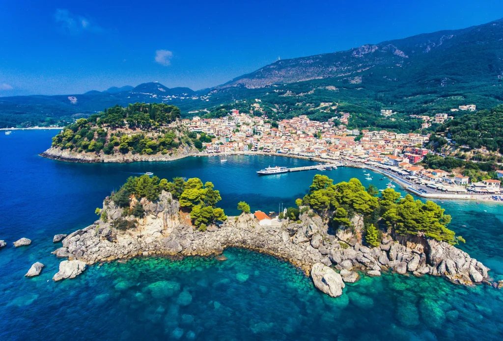 Vue aérienne de Parga, cité côtière parmi les plus belles de Grèce, avec eaux turquoise, collines boisées et maisons pastel perchées sur les hauteurs.