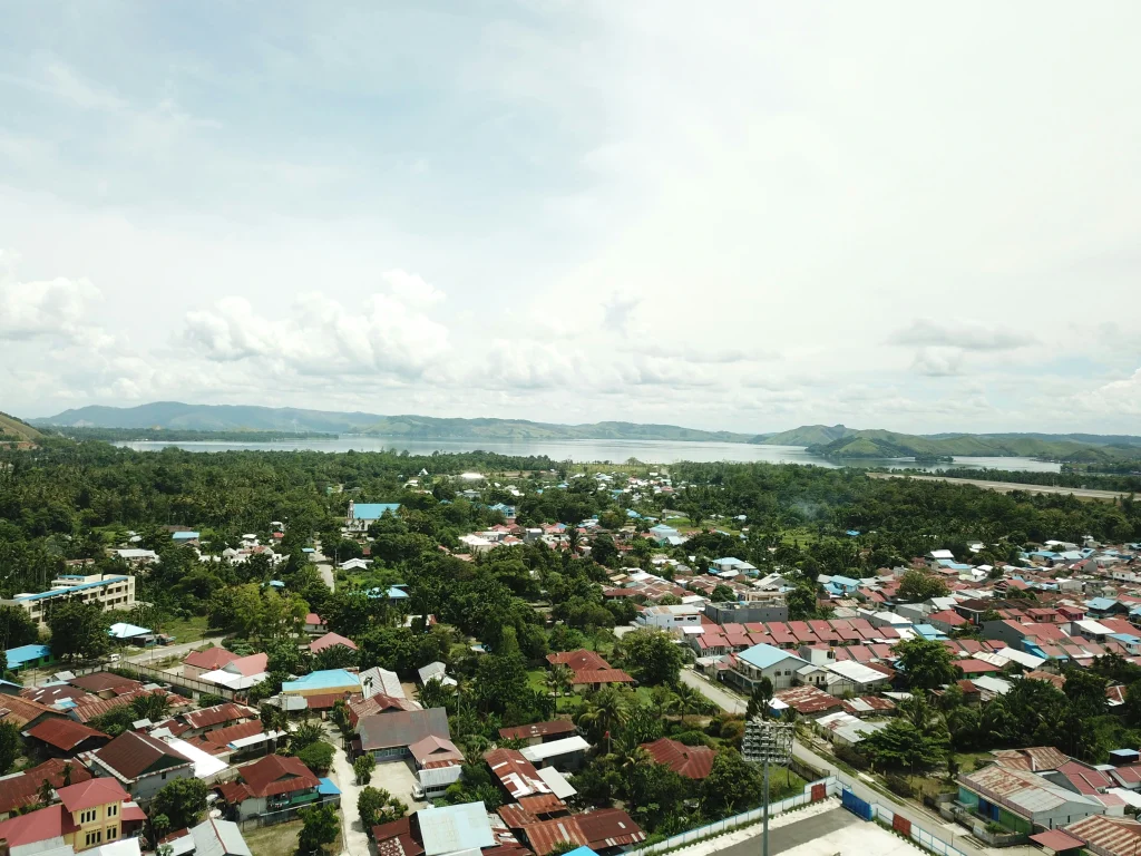 Aerial view of a Philippine city with housing surrounded by greenery and hills near the sea.