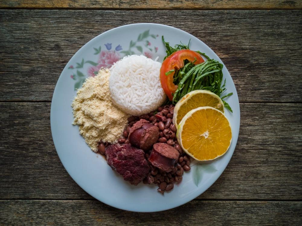 Traditional Brazilian feijoada plate with black beans, pork, rice, farofa, vegetables, and orange slices—an iconic dish of Brazil.