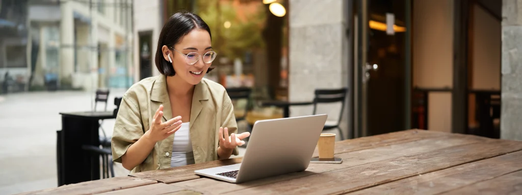 Femme travaillant à distance depuis une terrasse, discutant en visioconférence sur son ordinateur portable.