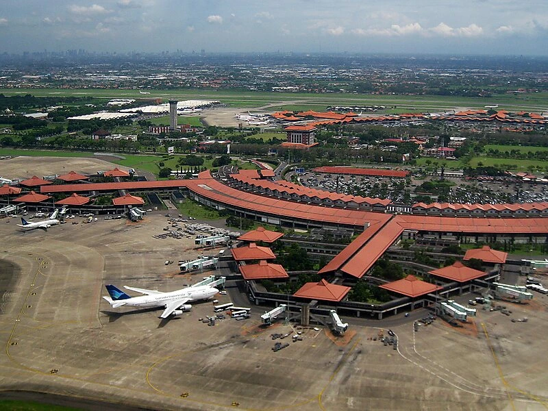 Vue aérienne d’un grand aéroport en Indonésie, avec terminaux aux toits rouges et plusieurs avions stationnés sur le tarmac.