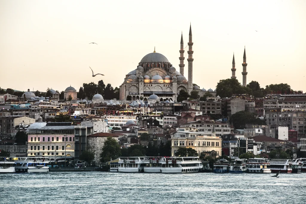 Vue d’Istanbul au coucher du soleil, avec une grande mosquée ottomane en arrière-plan et des bateaux naviguant sur le Bosphore.