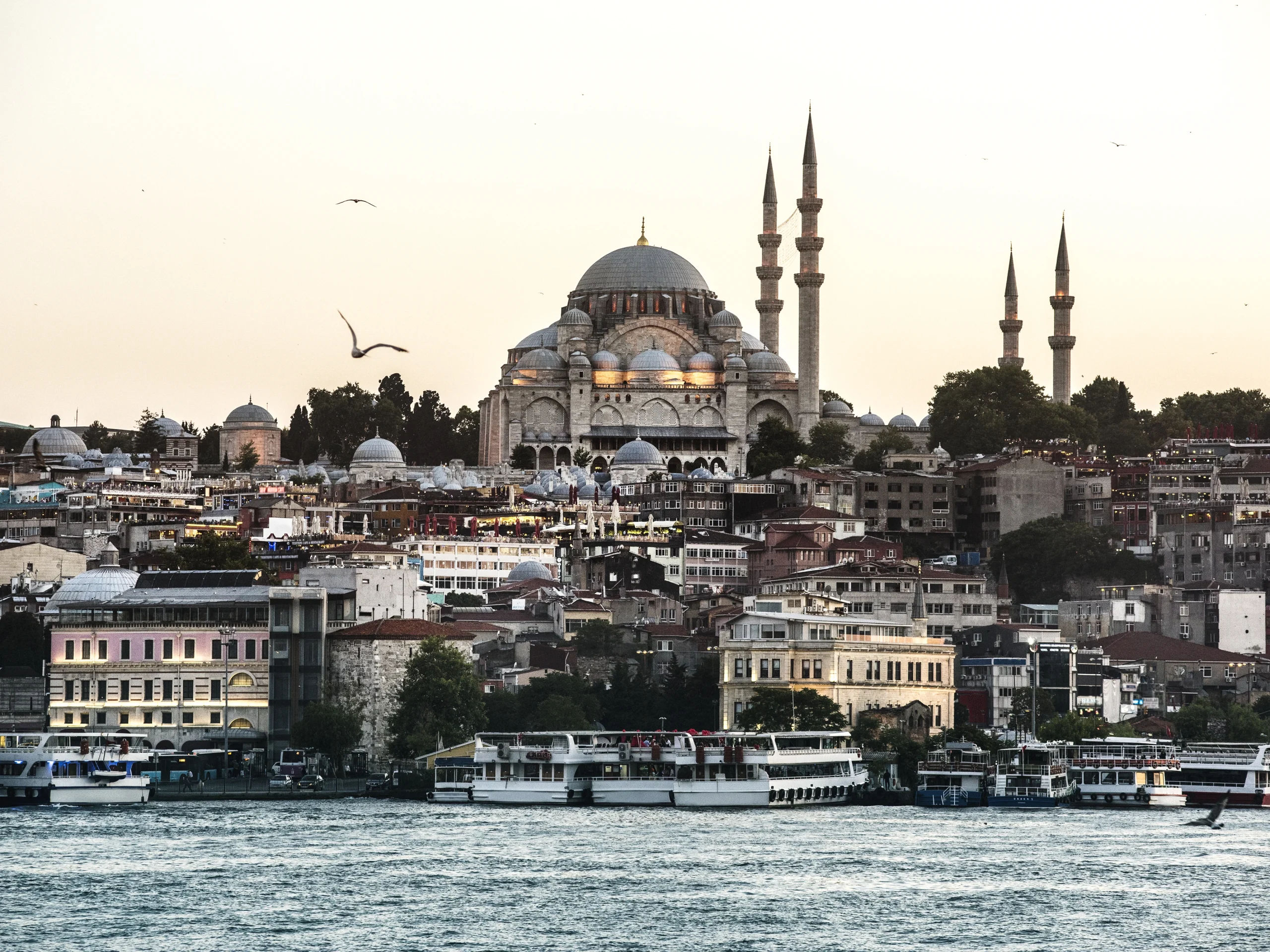 View of Istanbul at sunset, with a large Ottoman mosque in the background and boats sailing on the Bosphorus.